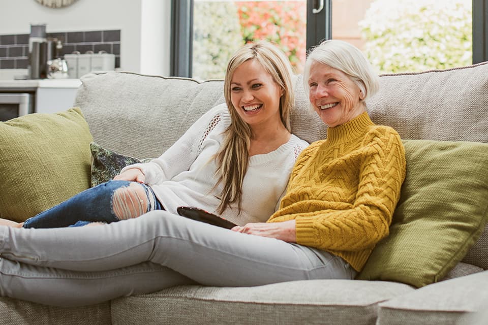Oma und Enkelin sitzen lächelnd auf dem Sofa