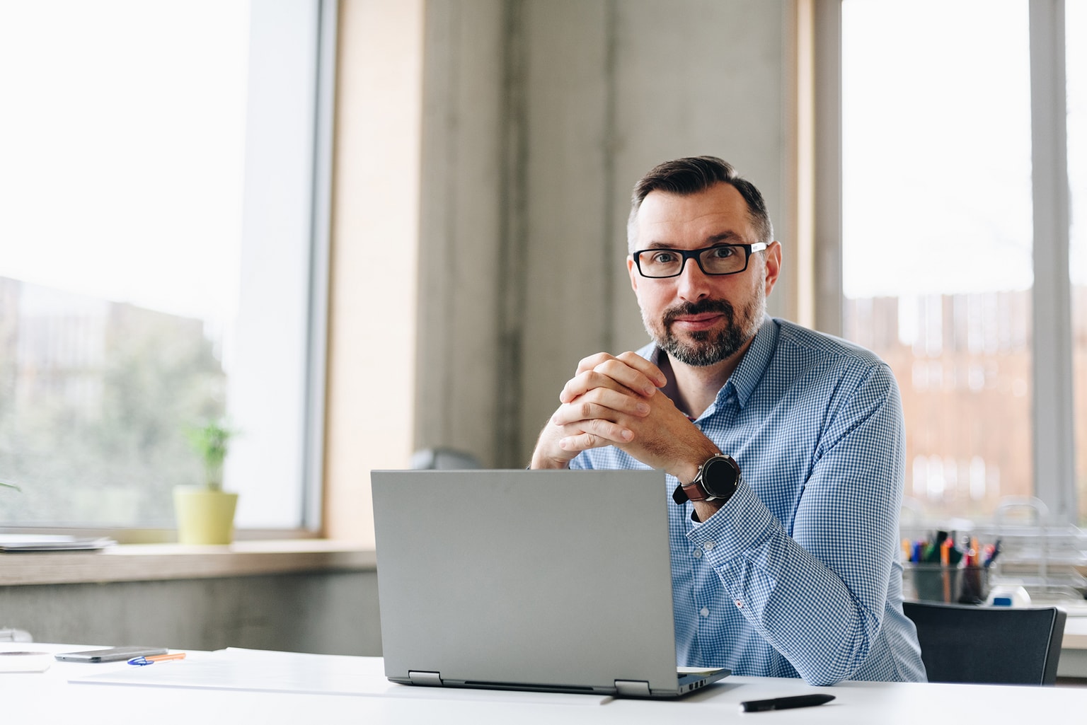 Business Mann sitzt im Büro mit großen Fenstern vor einem Laptop, Partnerprogramm Champions