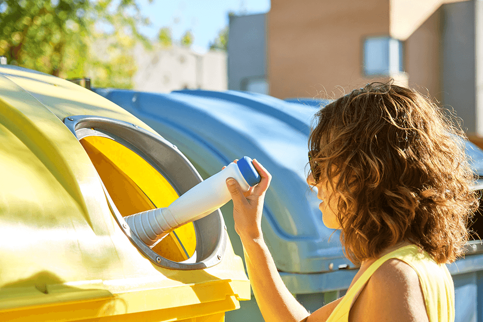 Frau trennt den Müll und wirft Plastik in den gelben Behälter
