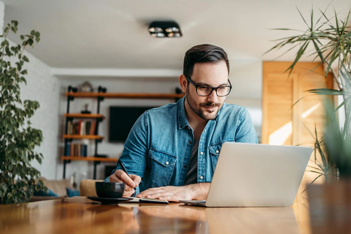 Mann sitzt am PC und macht sich Notizen in einem Block