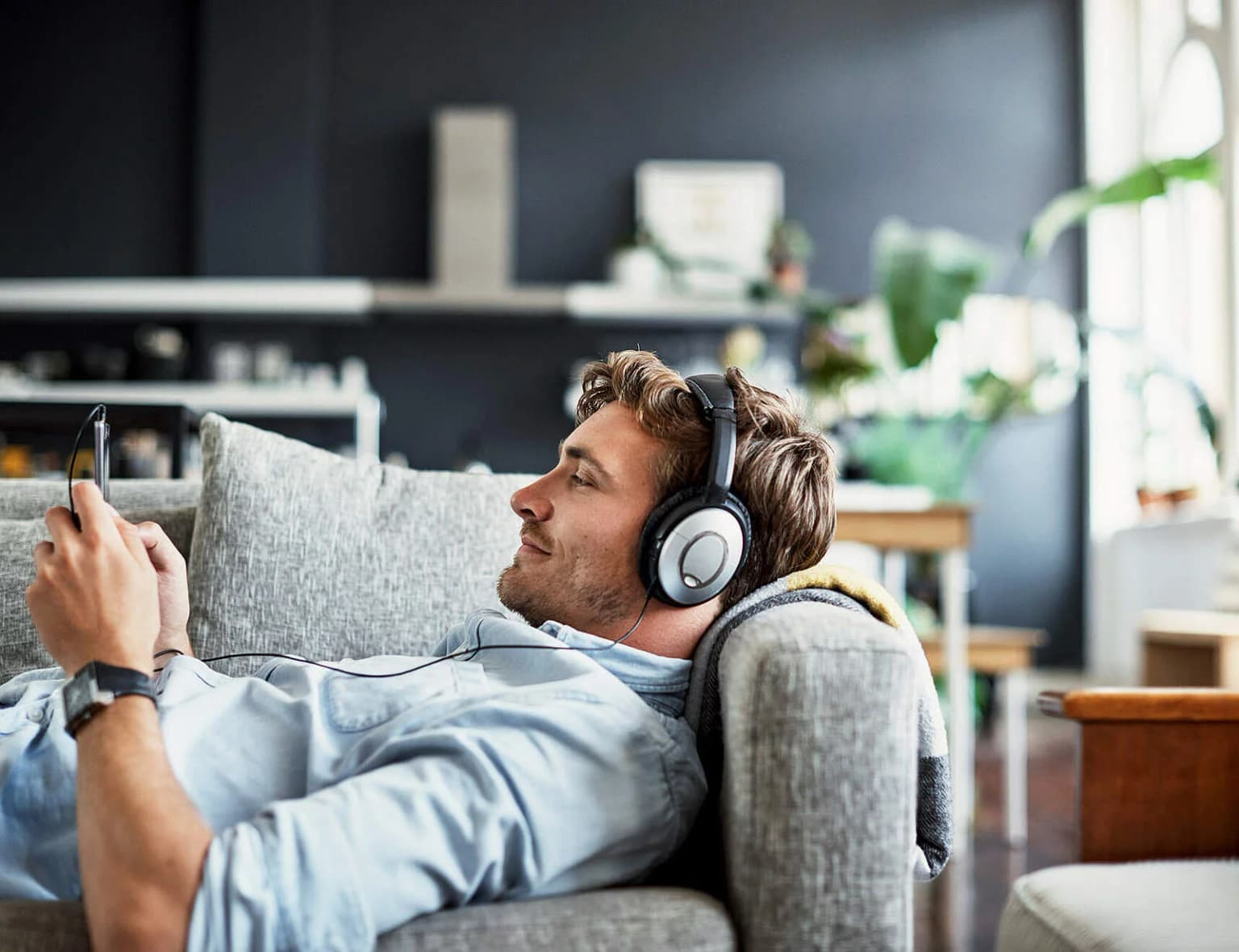 Mann liegt auf dem Sofa mit Kopfhörern und schaut auf sein Ha