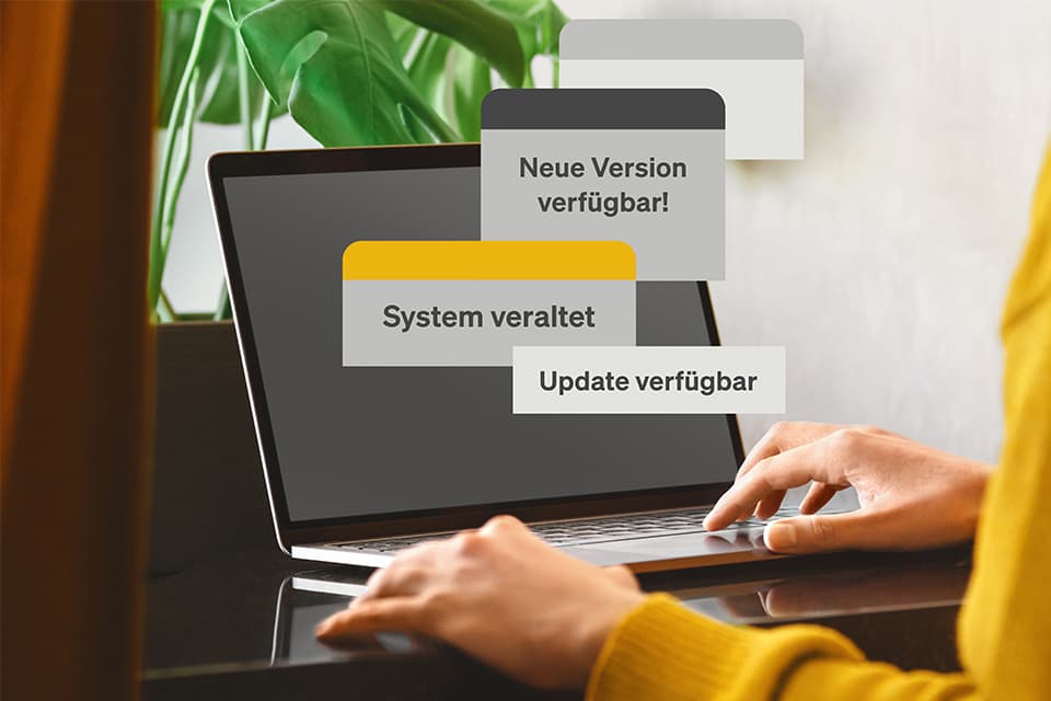 Person tippt auf Laptop, auf dem Hinweise erscheinen: „Neue Version verfügbar", „System veraltet" und „Update verfügbar".