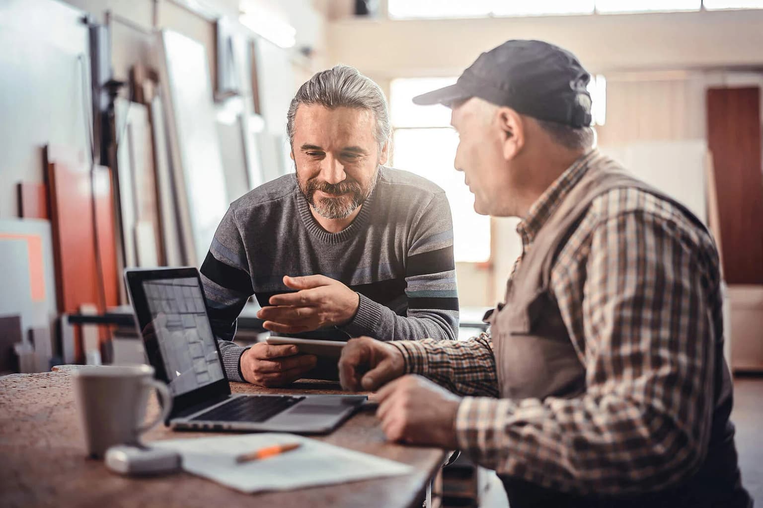 B2B Handwerker sitzen in der Werkhalle am Laptop und unterhalten sich