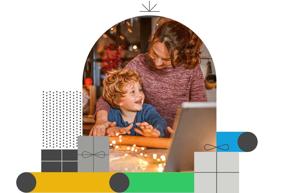 Frau und Kind sitzen gemeinsam vor einem Laptop in gemütlicher Weihnachtsatmosphäre mit Lichterketten im Hintergrund.