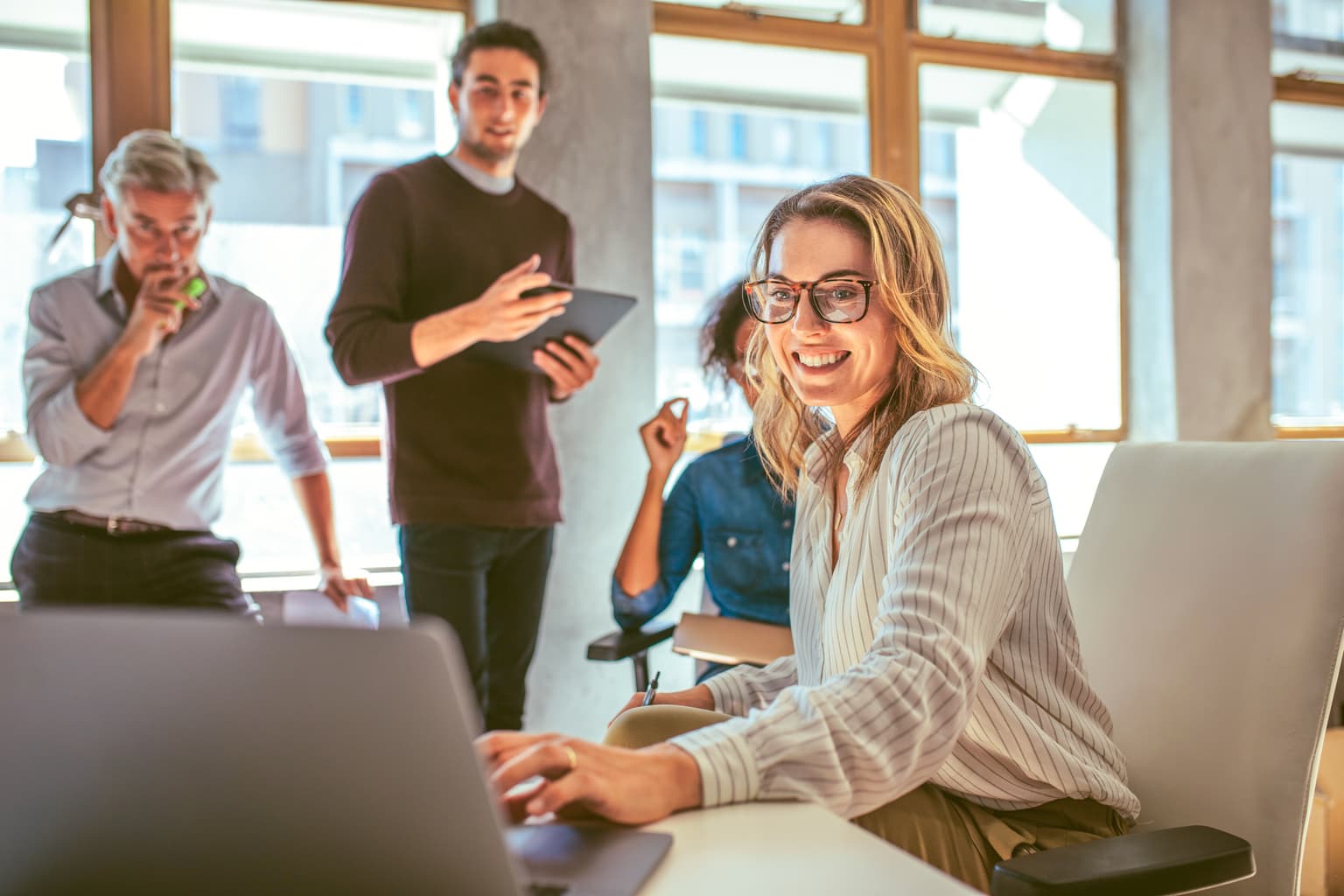 Team sitzt im Büro und Frau präsentiert ihr Projekt am Laptop - Digitale Transformation