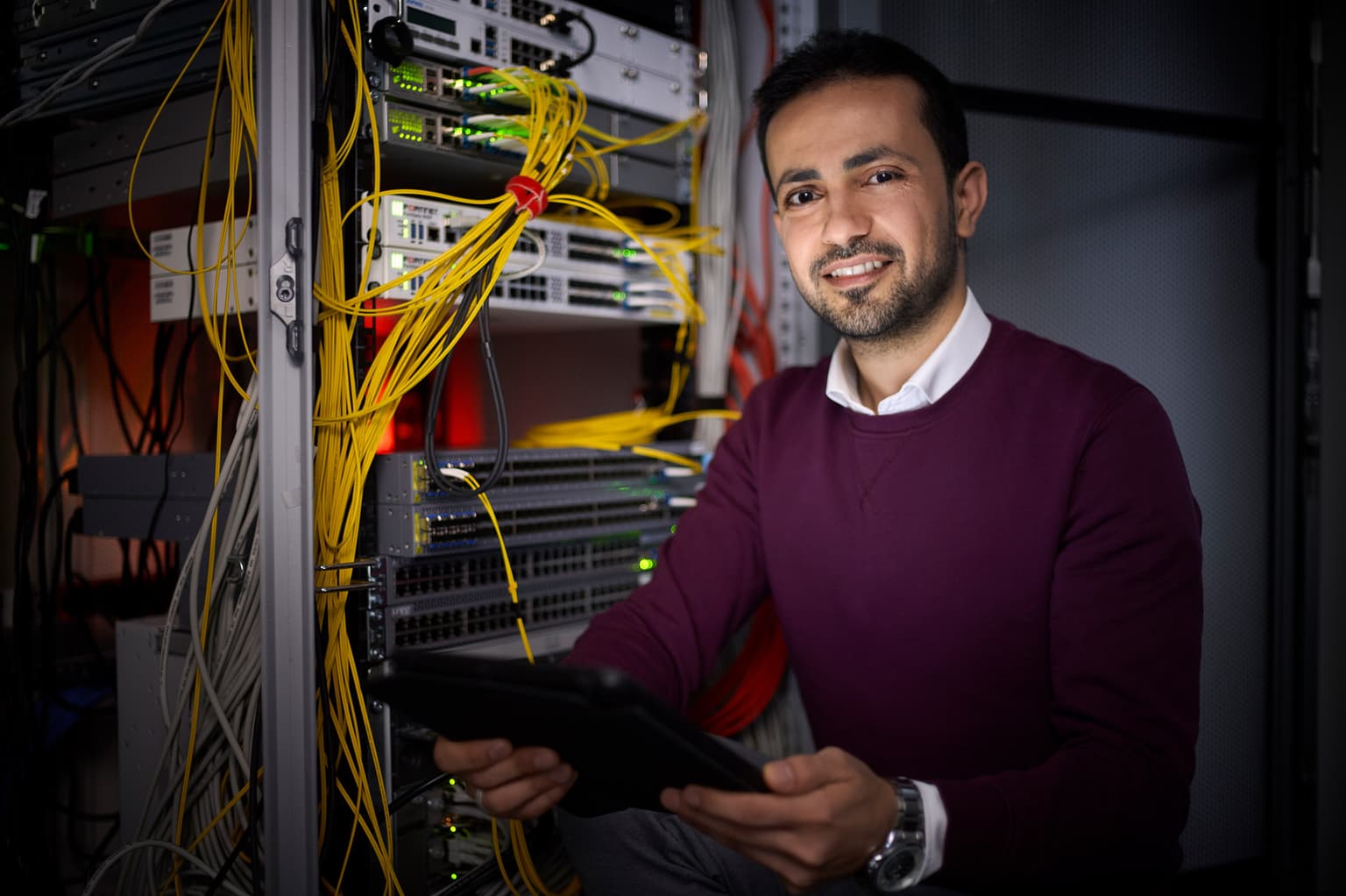 Das Bild zeigt eine Person, die ein Tablet in der Hand hält und sich in einem Serverraum befindet.