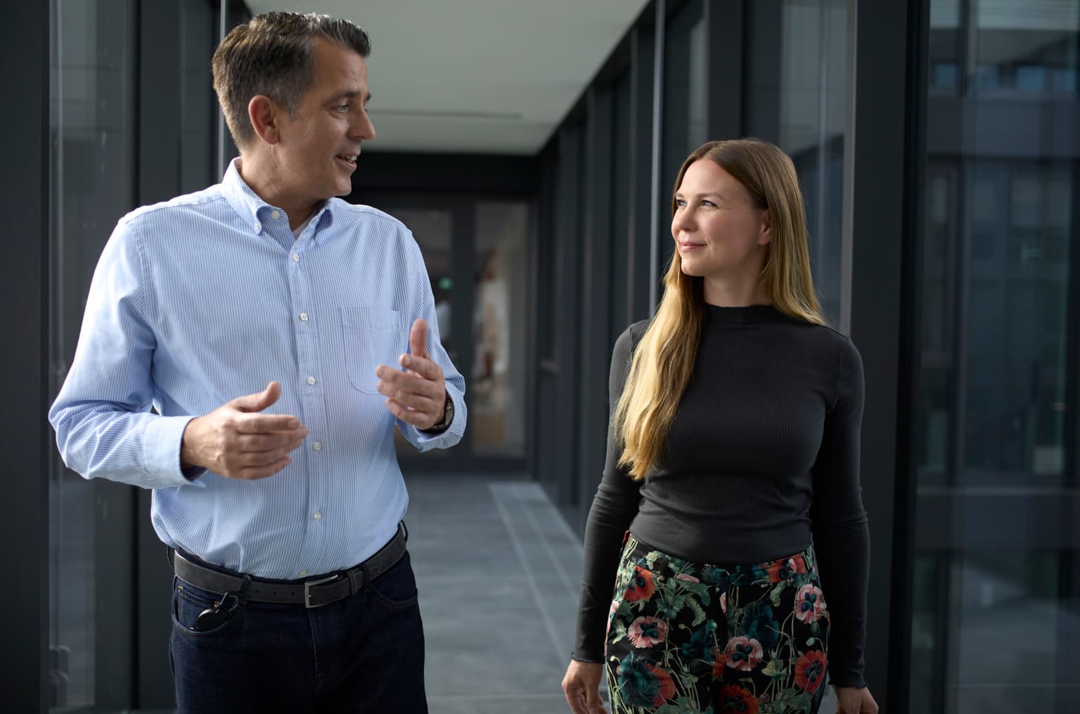 Das Bild zeigt zwei Personen, die durch das Büro laufen und sich unterhalten.