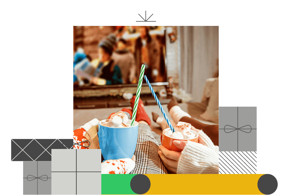 Gemütliche Szene mit zwei Tassen heißer Schokolade mit Sahne und bunten Strohhalmen vor einem unscharfen Fernseher.