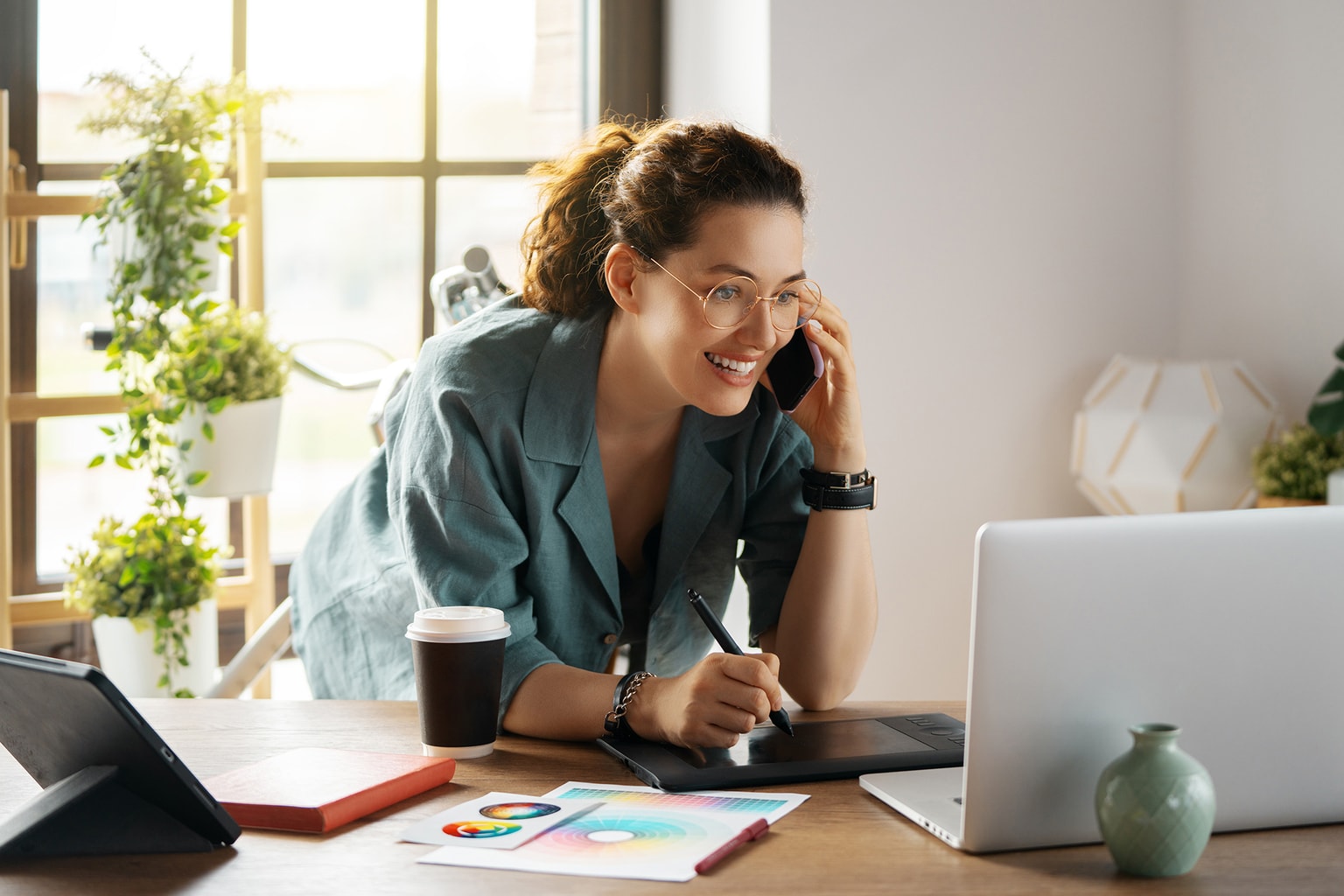 Die Frau telefoniert, während sie am PC arbeitet.