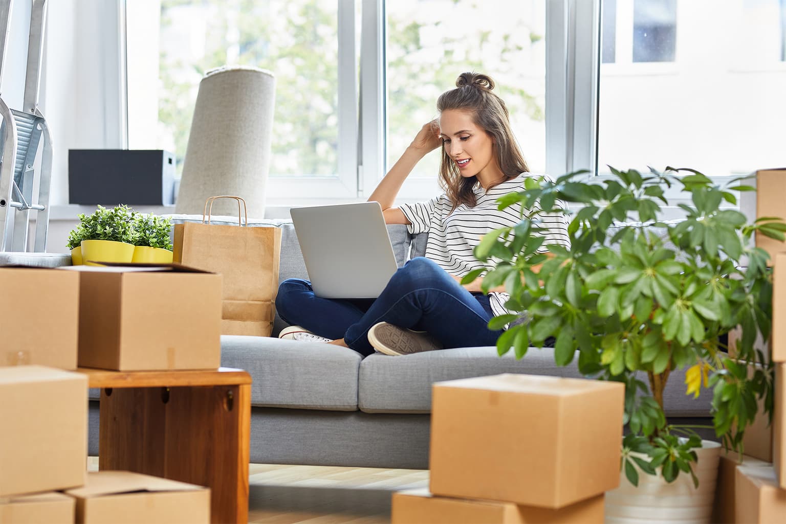 Service kündigen, Frau sitzt zwischen Umzugskarton und arbeitet am Laptop