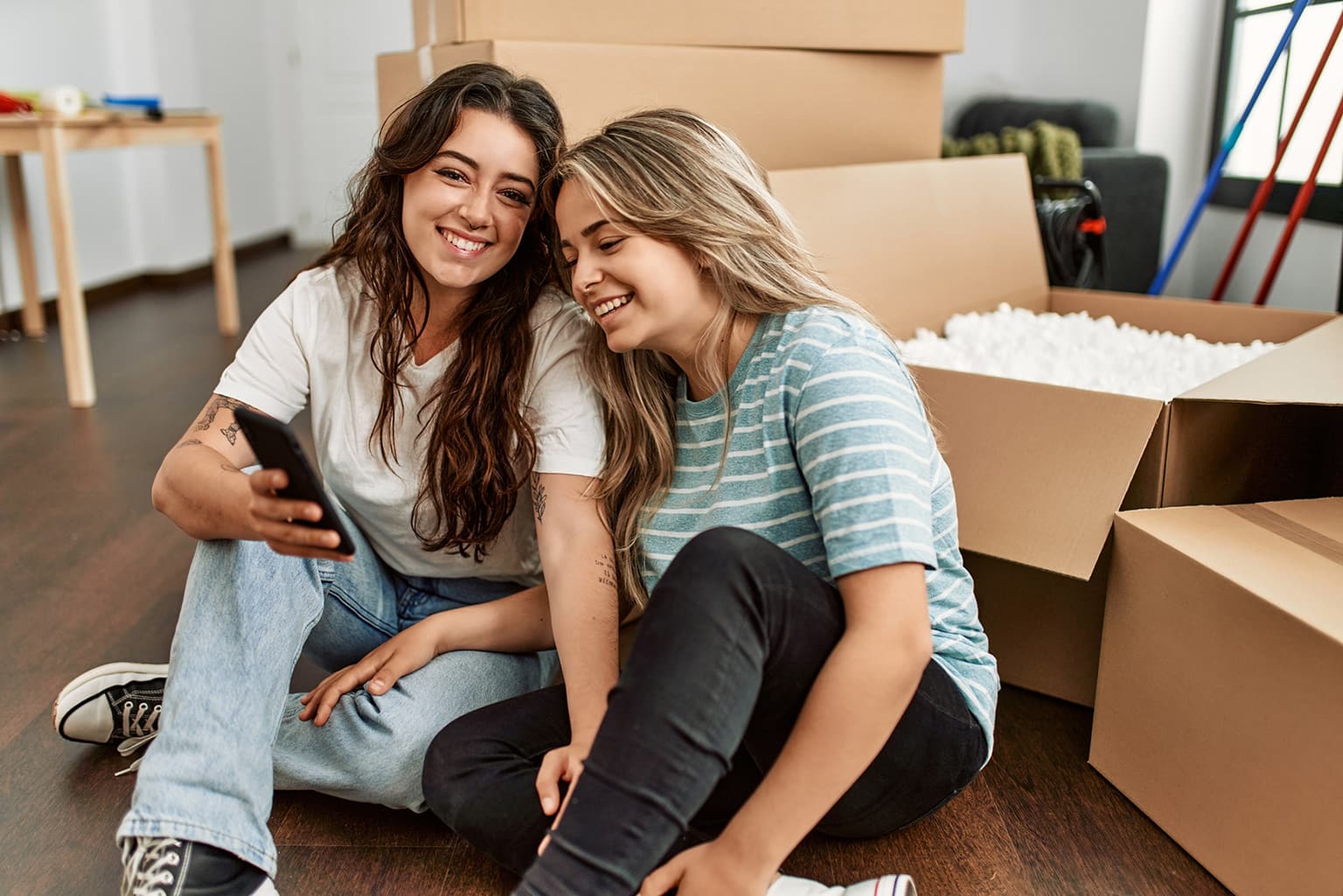 Umzug kündigen, Frauen sitzen auf dem Boden zwischen Umzugskartons