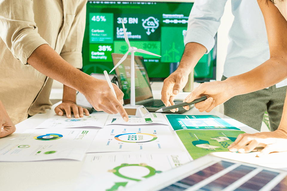 Verschiedene Personen halten ein Meeting über das Thema Nachhaltigkeit und schauen auf ausgedruckt Diagramme