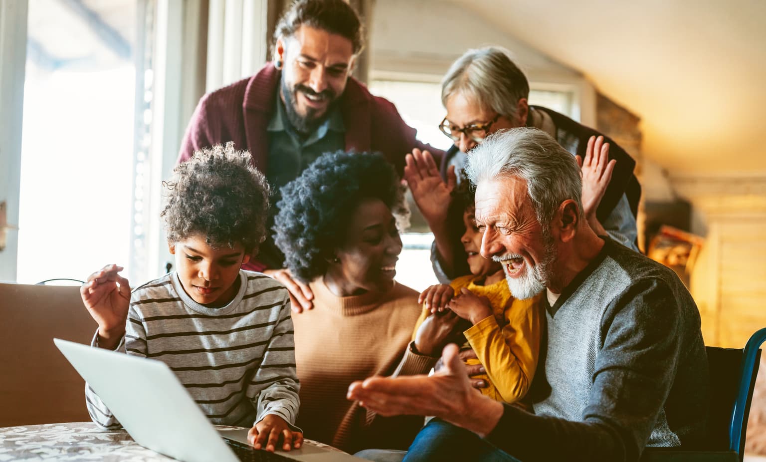 Eine Familie von sechs Personen befinden sich in einem Innenraum, vermutlich einem Wohnzimmer, und versammeln sich um einen Laptop. Einige zeigen oder gestikulieren in Richtung des Bildschirms. Die Gruppe wirkt konzentriert auf das Gerät.