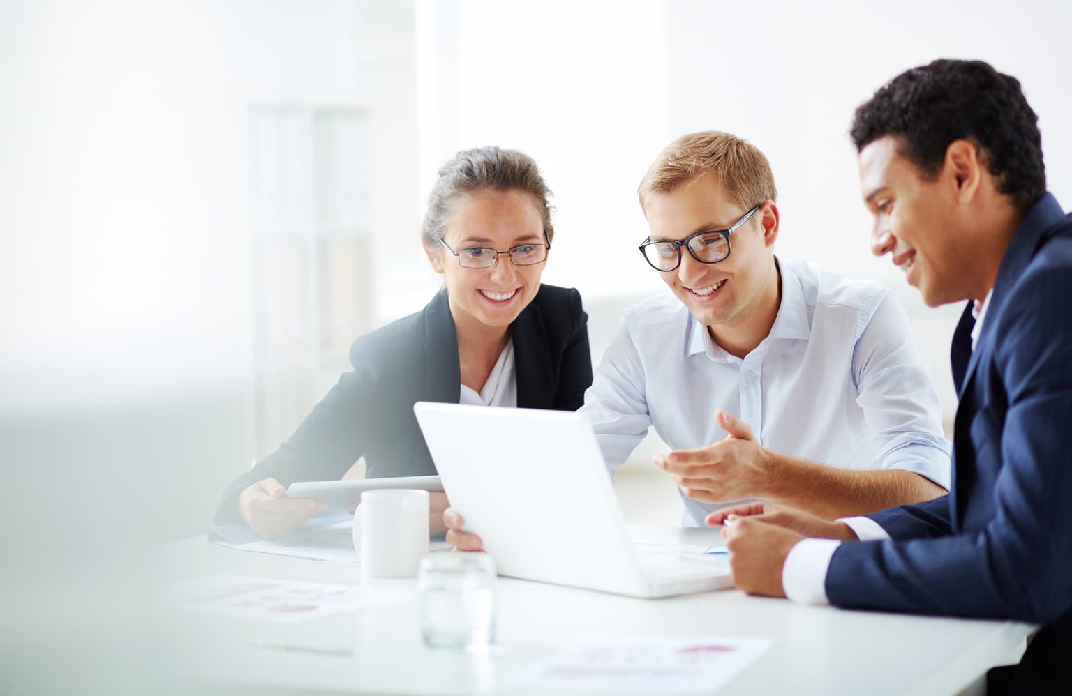 Drei Arbeitskoleg*innen sitzen im Büro am Tisch und besprechen den Inhalt auf dem Laptop