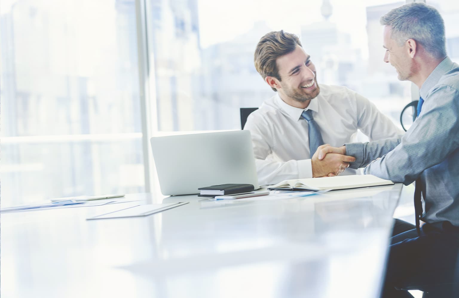 Schnell zum eigenen Glasfaseranschluss, Vermieterdaten, Zwei Männer geben sich die Hände im Büro