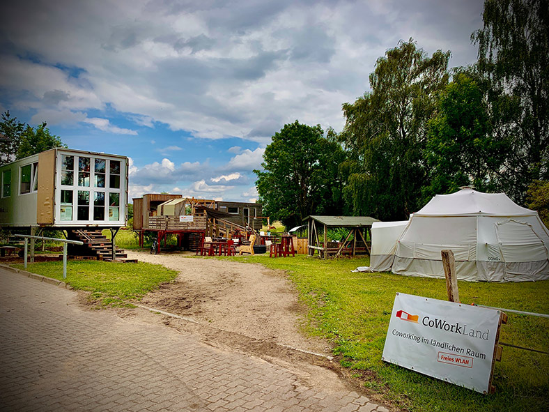 Zelte, Container und Tiny Houses und eine Tafel mit der Aufschrift „Coworkland – Coworking im ländlichen Raum. Freies WLAN“