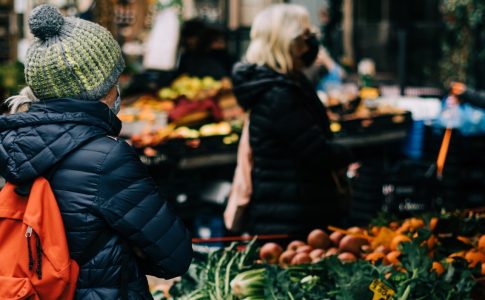 Marktstand mit frischem Obst und Gemüse und Kundinnen.