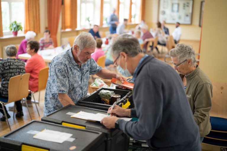 In einem großen Saal packen drei Personen Boxen mit Lebensmitteln aus.