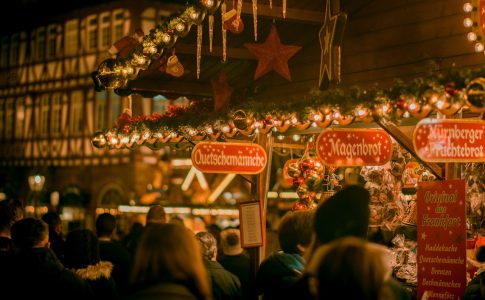 Ein Weihnachtsmarktstand verkauft Süßigkeiten, davor stehen und gehen Passanten.