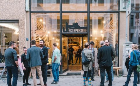 Personen stehen in einer Fußgängerzone vor der gläsernen Fassade eines Geschäfts.