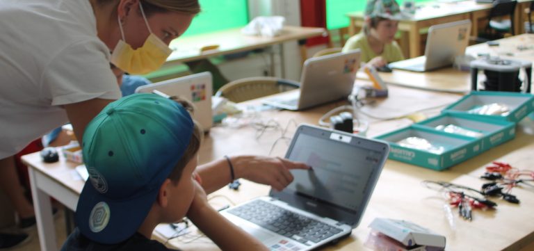 An einem Tisch sitzt ein Junge vor einem Laptop. Eine Frau deutet mit ihrem Finger auf den Bildschirm.