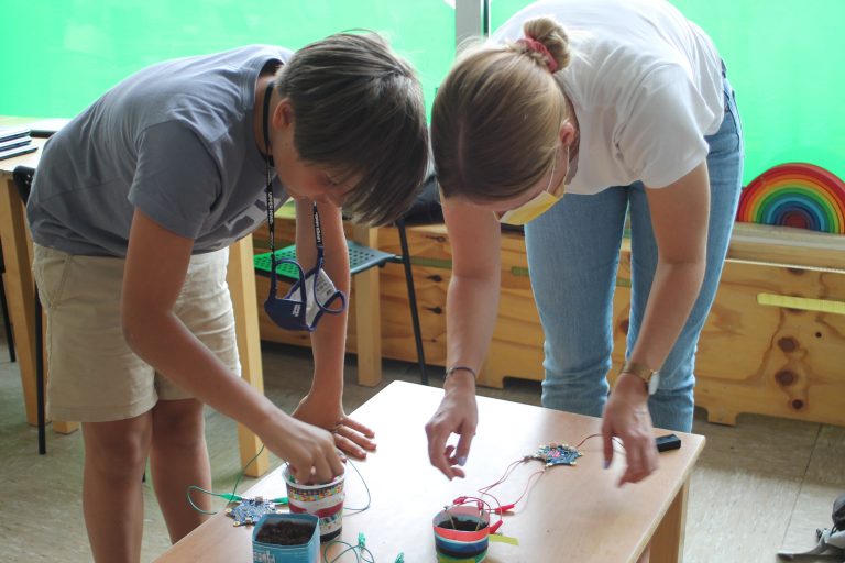 Zwei Jugendliche beugen sich über einen Tisch mit Kabeln und elektronischen Bauteilen.