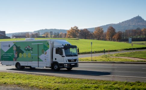 Ein grün beklebter Laster fährt über eine Landstraße.