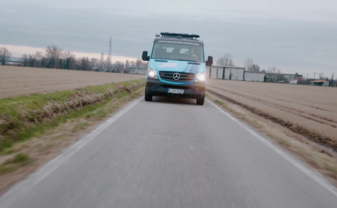 Ein türkisfarbener Van rollt über eine Landstraße.