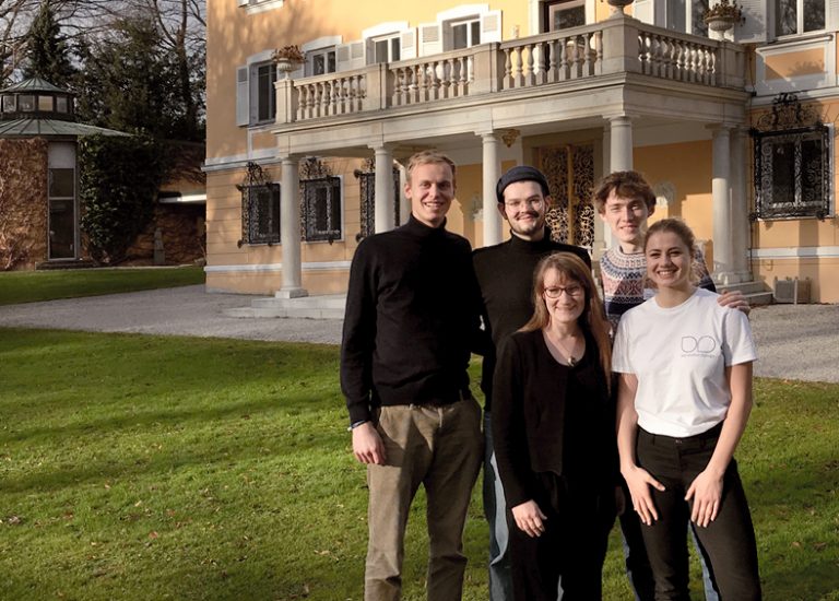 Fünf Personen stehen auf einer grünen Wiese, dahinter ist das gelbe Schloss Tutzing zu sehen.