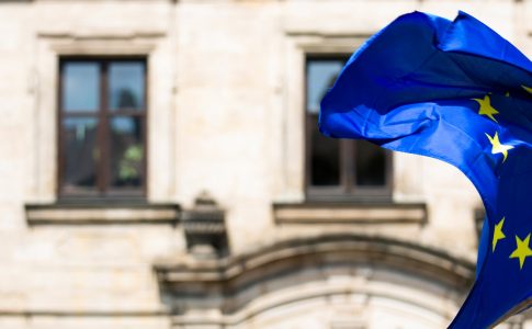 Vor einem Sandsteingebäude weht die europäische Flagge im Wind.