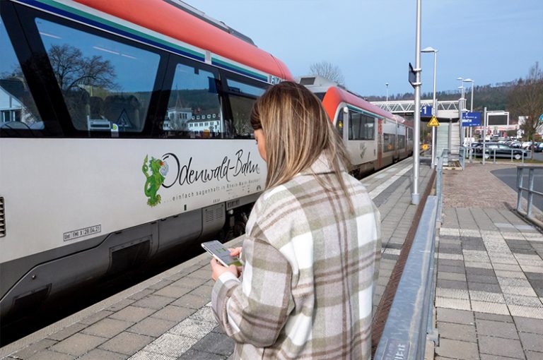 Eine Frau steht auf einem Bahnsteig, an dem die Odenwald-Bahn wartet.