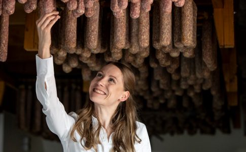 eine Frau steht in einem Raum, in dem Trockenwürste von der Decke hängen.