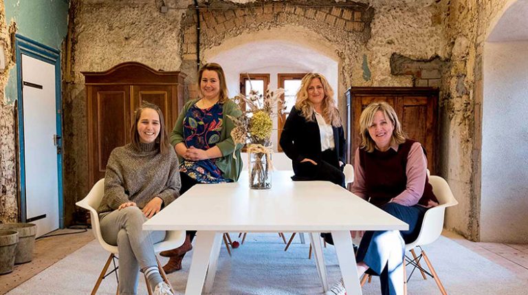 Ein weißer Tisch steht in einem Raum mit dicken, unverputzten Wänden. Vier Frauen sitzen am Tisch.
