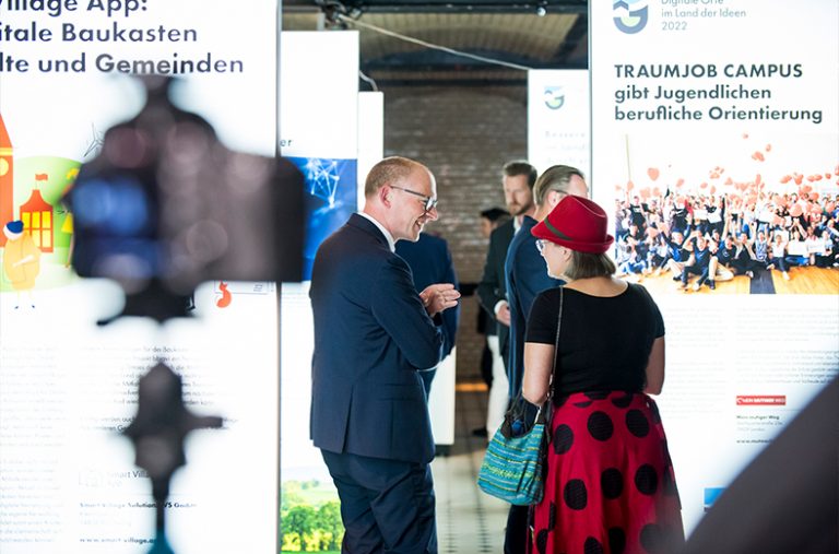 Eine Frau und ein Mann unterhalten sich vor beleuchteten Ausstellungstafel