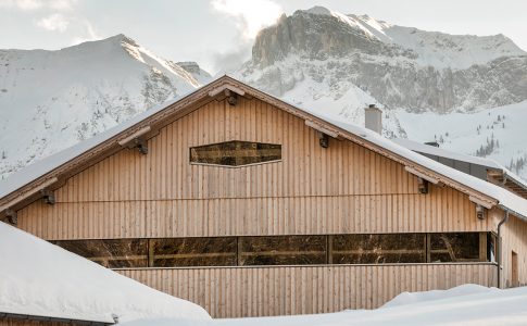 Ein Bauernhof in den Bergen vor verschneiter Kulisse.