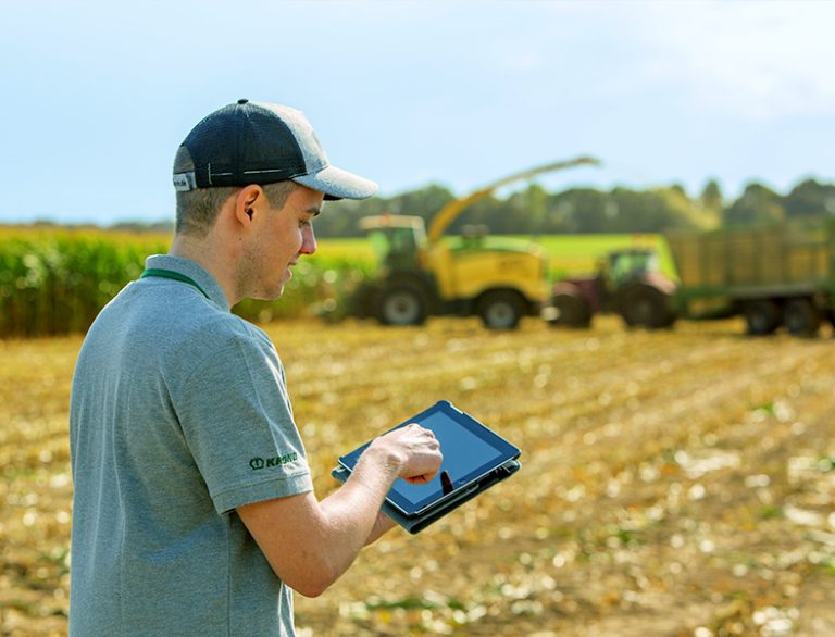 Ein junger Mann mit Baseballcap steht mit Tablet auf einem Feld.