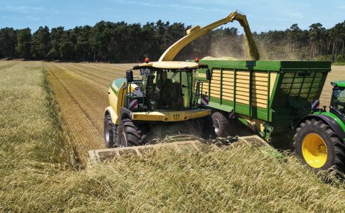 Zwei Landmaschinen der Marke Krone bei der Ernte auf einem sommerlichen Feld.