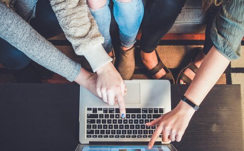 Mehrere Menschen zeigen mit ihrem Finger auf einen Laptop-Bildschirm.