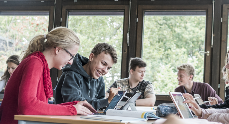 Mehrere Schüler:innen, die in einem Klassenraum an Tablets arbeiten.