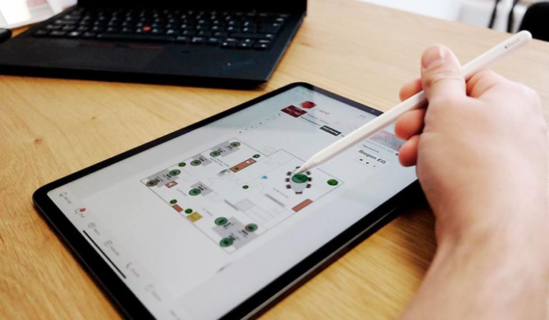 Hand tippt mit Stift auf Tablet-Bildschirm mit schematischer Raumübersicht.