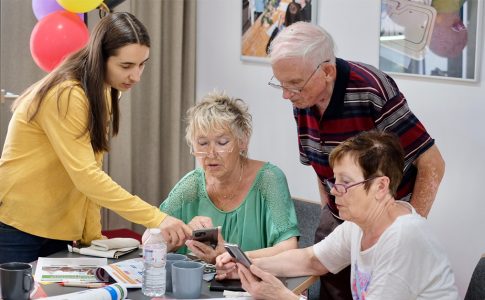 Ein jüngerer Mensch zeigt drei älteren Menschen etwas auf dem Smartphone.