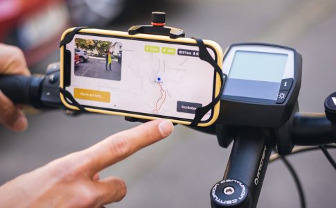 Ein Finger zeigt auf ein Smartphone, das am Fahrradlenker befestigt ist.