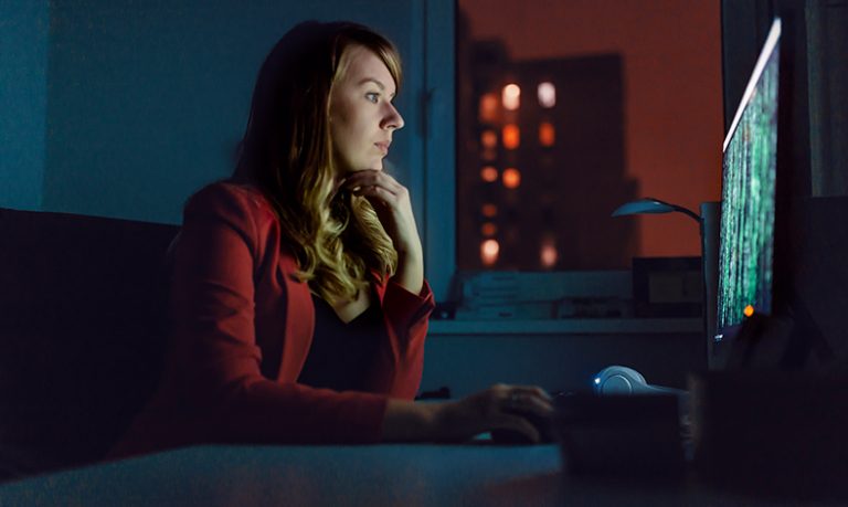 Frau sitzt im Dunkeln vor einem beleuchteten Bildschirm.