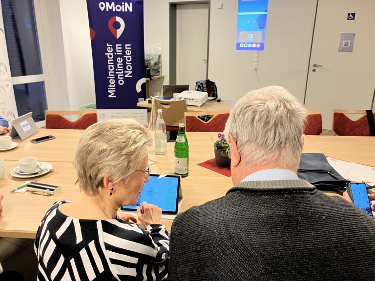 Seniorin und Senior sitzen vor Tablets an einem Tisch.