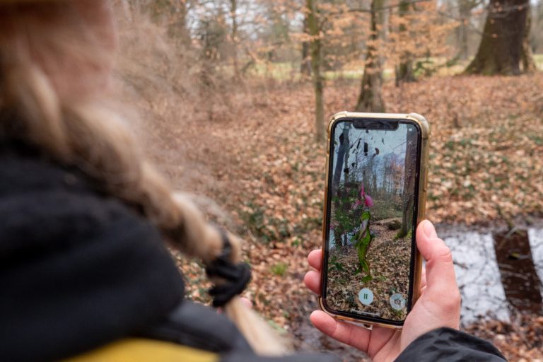 Eine Frau hält im Wald ein Handy in der Hand. Foto Naturpark Hoher Fläming e.V.