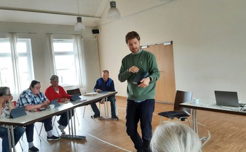 Björn Kuhlenkamp mit Tablet in der Hand vor einer Gruppe von Senior:innen.