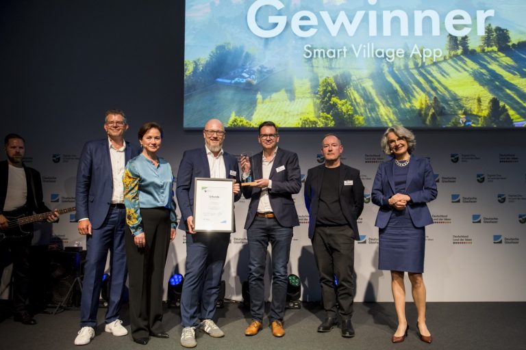 Fünf Personen auf einer Bühne, ein Preisträger hält eine Urkunde in der Hand. Foto: Deutschland – Land der Ideen/Bernd Brundert