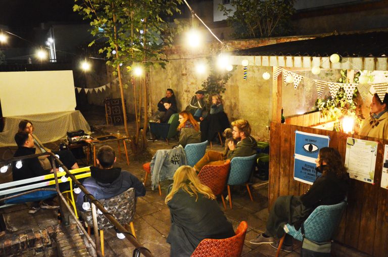 Stimmungsvoll beleuchteter Hinterhof bei Nacht mit Menschen auf Stühlen