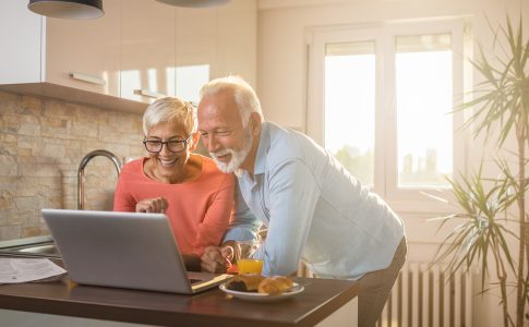 Älteres Ehepaar steht vor einem aufgeklappten Laptop auf der Küchenzeile.