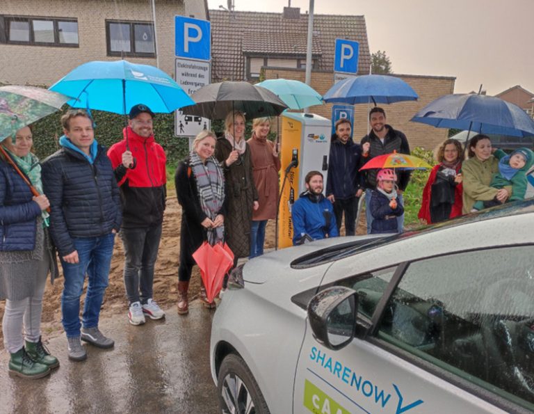 Menschen mit Regenschirmen stehen vor einem Carsharing-Auto.